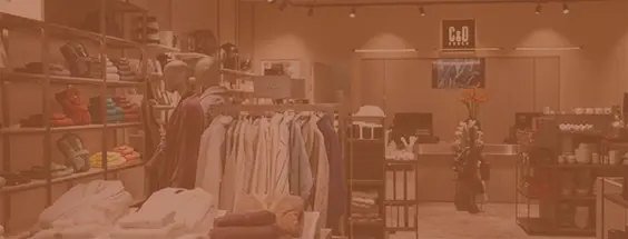 Clothing store interior with racks of shirts and folded garments; checkout area visible in the back.